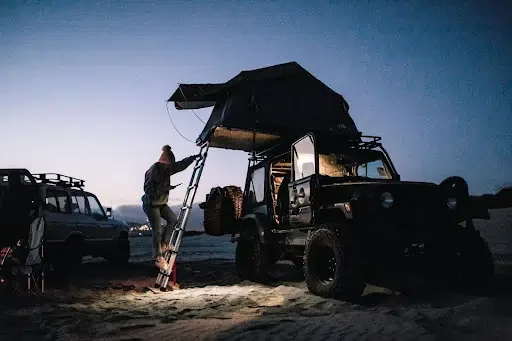 A jeep with a rooftop tent on a beach at sunset; an ideal car camping setting.