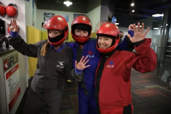 Three women wearing flight suits, ready to try indoor skydiving.