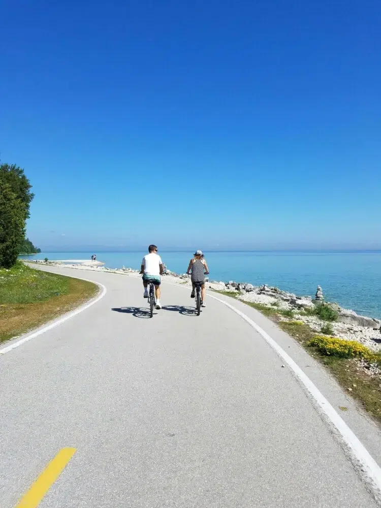 2 people riding bikes on a shore because biking is a great way to relax your mind on vacation