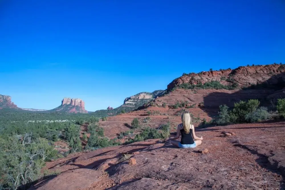 Woman meditating on the red rocks of Sedona, AZ. One of the travel habits that improve your wellbeing.