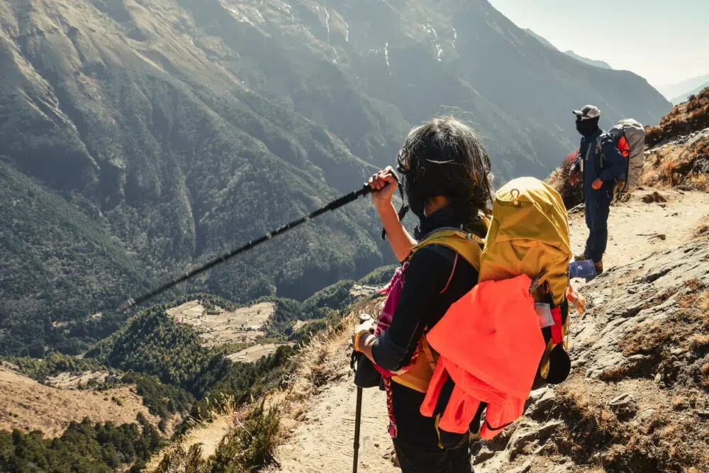 Caucasian woman trekker with male guide stand treks on path high viewpoint in Sagarmatha national park. EBC trekking. Everest base camp trekking in fall, autumn in sunny weather