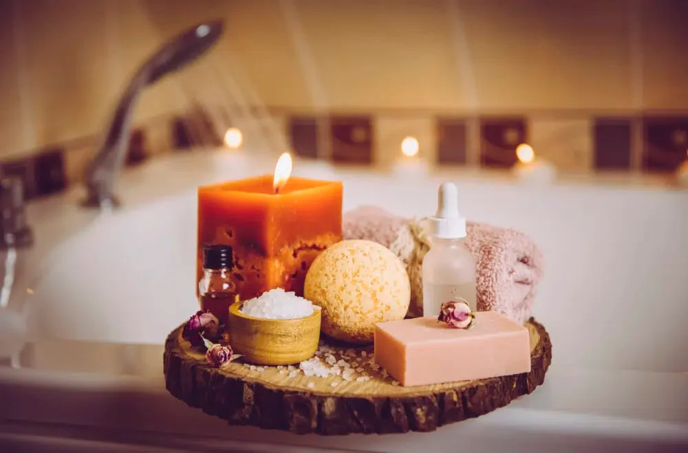 home spa products on a wooden tray; soap, bath bomb, bath salt, essential oils and burning candle, perfect for hotels with in-room hot tubs.